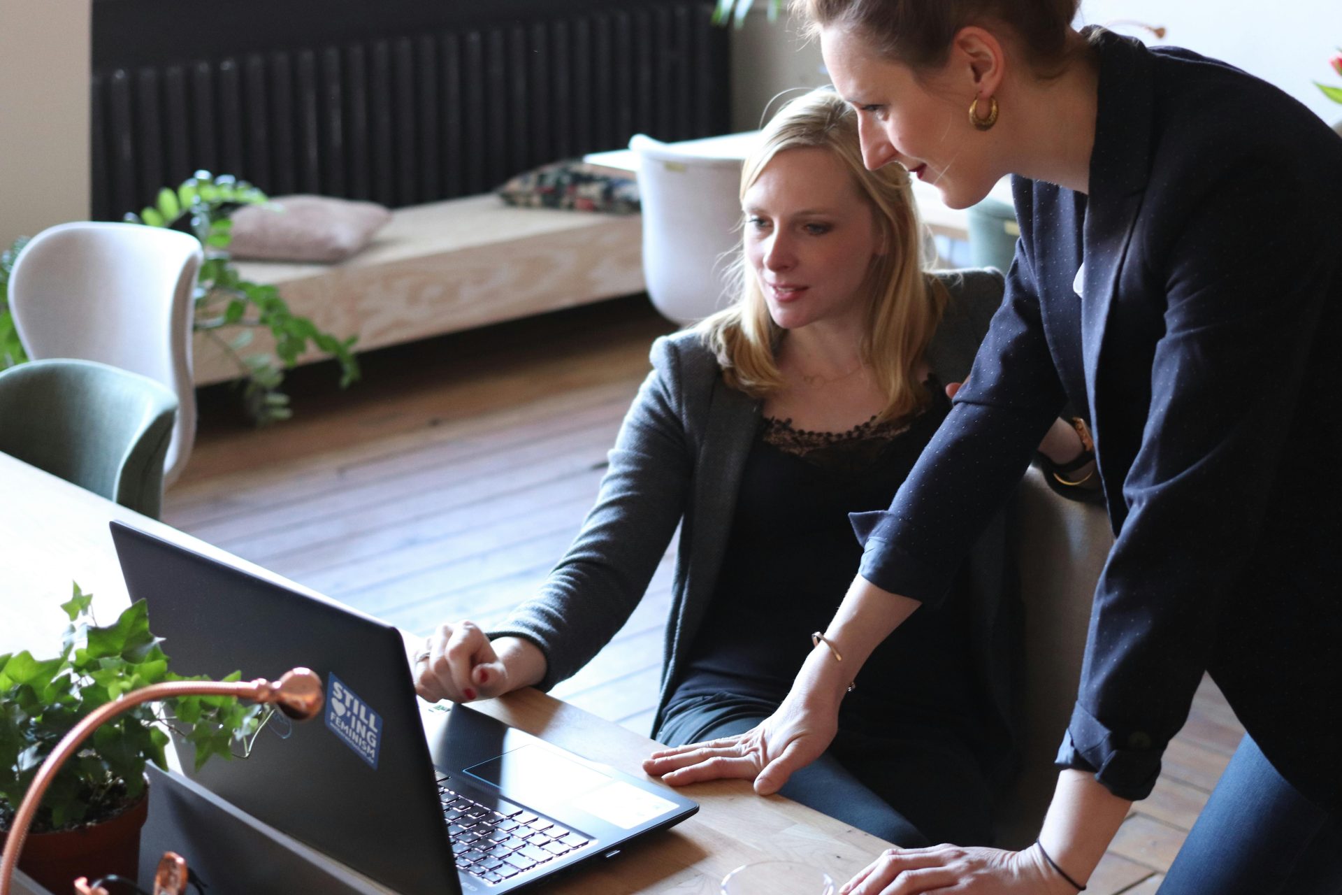Zwei berufstätige Frauen besprechen ein Projekt mithilfe eines Laptops in einer modernen Büroumgebung.